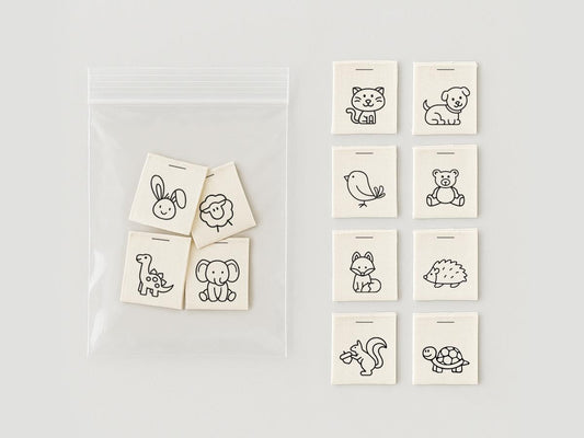 May include: A collection of small, off-white fabric tags with black line drawings of various animals, including a cat, dog, bird, bear, fox, hedgehog, squirrel, and turtle. Some tags are in a clear plastic bag.