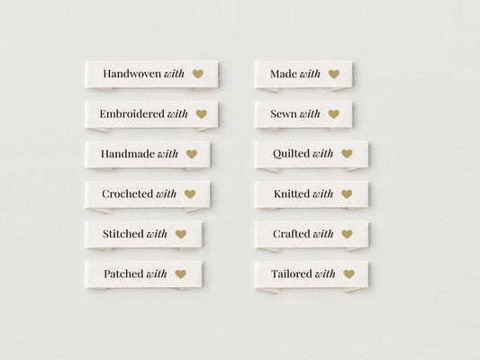May include: A collection of off-white fabric labels with gold text and a gold heart icon. The labels read: Handwoven with, Embroidered with, Handmade with, Crocheted with, Stitched with, Patched with, Made with, Sewn with, Quilted with, Knitted with, Crafted with, and Tailored with.